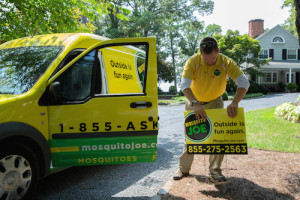 Mosquito Joe tech placing sign in yard next to parked Mosquito Joe van